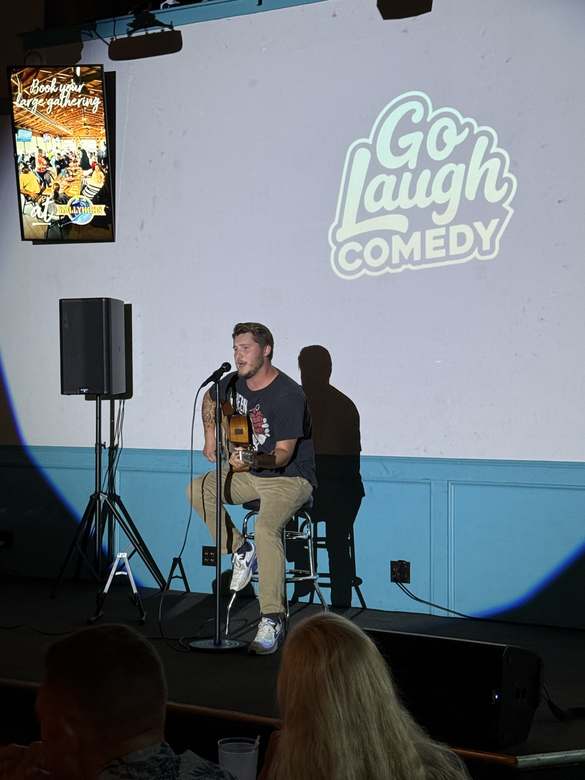 Comedian playing guitar on stage at Ballyhoos