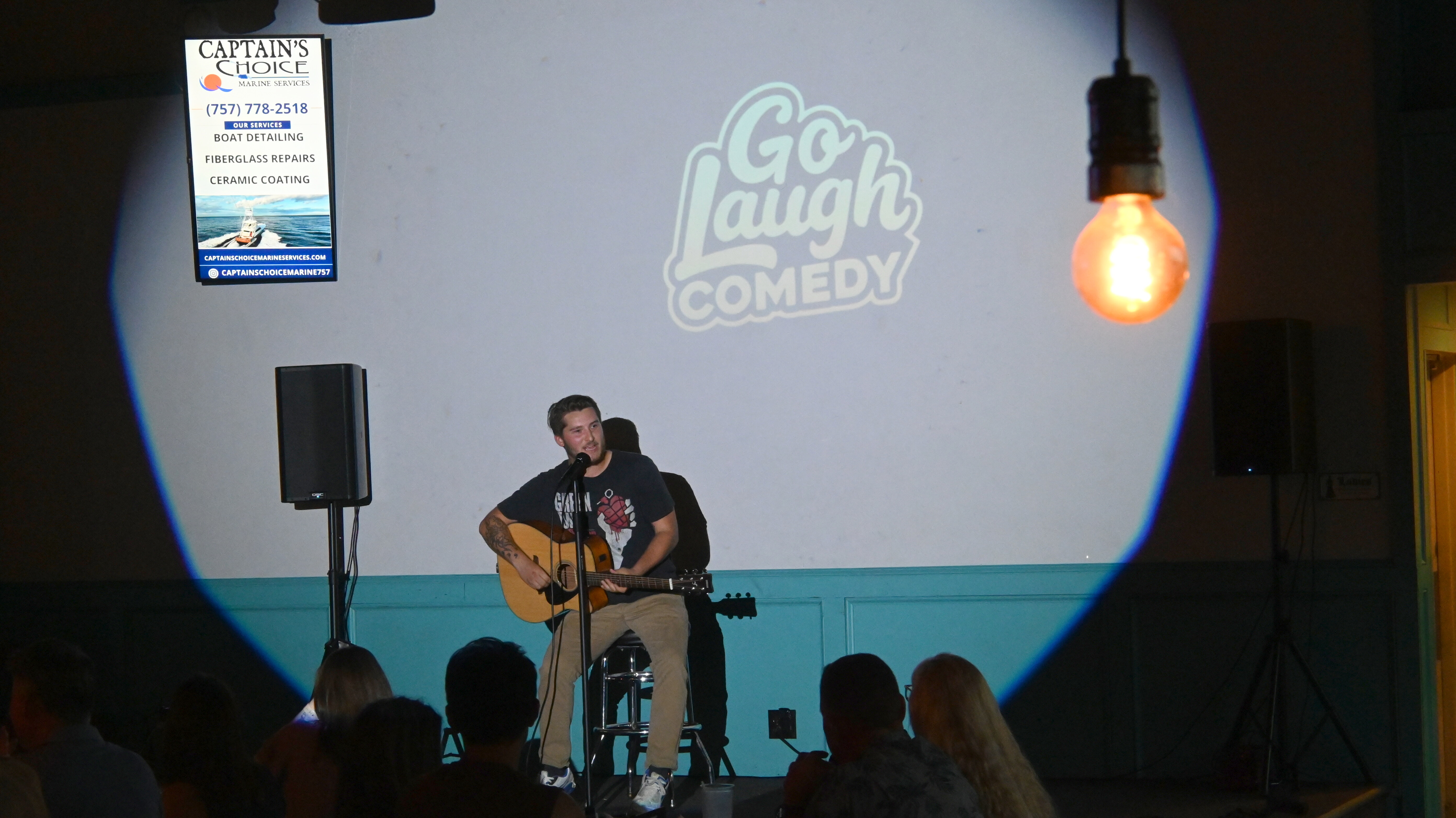Comedian playing guitar on stage at Ballyhoos