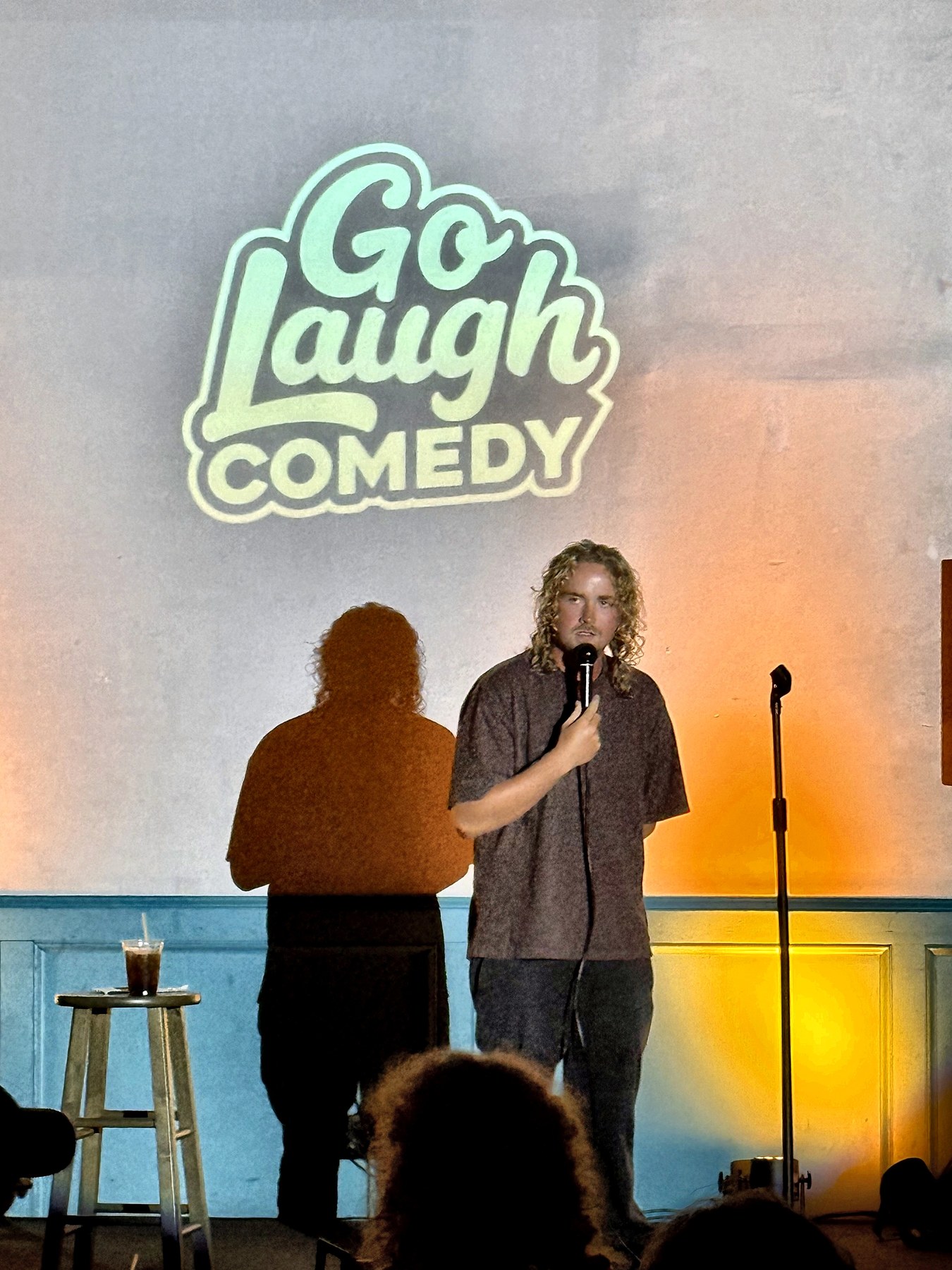 Comedian performing on stage under the Go Laugh Comedy logo at Ballyhoos