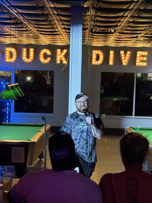 Comedian performing under the Duck Dive marquee lights