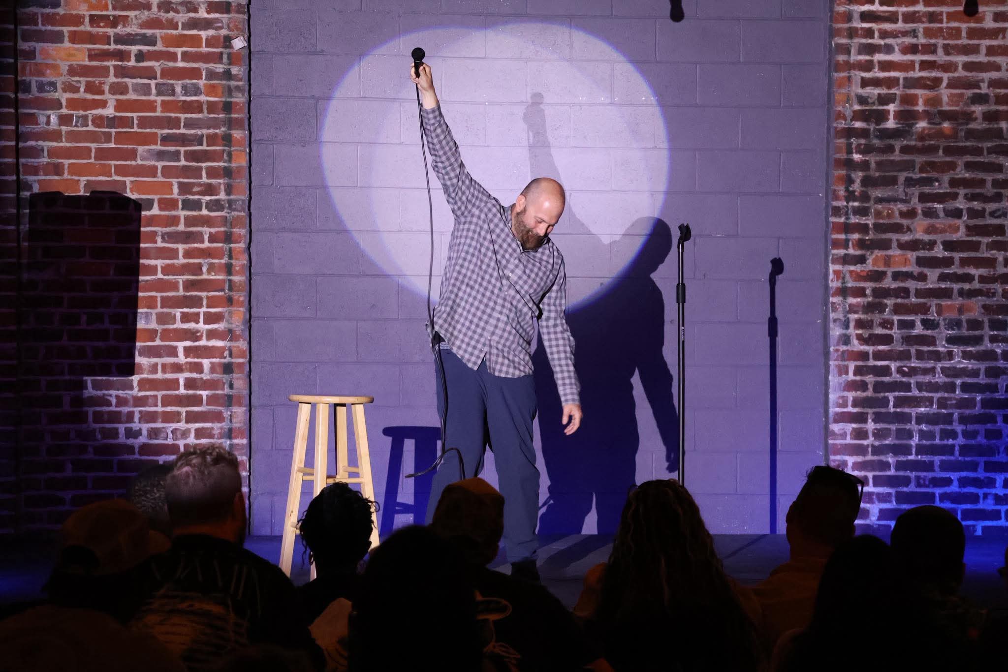 Comedian raising the mic on stage at Maker's Craft Brewery
